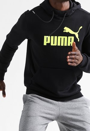 Sort hættetrøje lavet af blødt stof med en stor, lys gul PUMA-logo på forsiden. Indeholder snore til hætten og en kængurulomme.