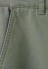 Olivově zelená látka s přímým švem, hladkou texturou a zesíleným šitím, typická pro kalhoty nebo šortky.