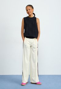Black sleeveless top with textured squares, paired with cream wide-leg pants featuring maroon side stripes and pink slip-on shoes.
