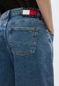 Tommy Jeans šviesiai mėlynos spalvos džinsai su lipduku juosmens juostoje, kurioje yra raudonos, baltos ir mėlynos spalvos. Drobės audinyje - susidėvėjimo efektas.