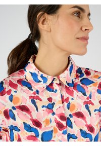 Blusa con colletto in un tessuto leggero, caratterizzata da un motivo astratto colorato con macchie di rosa, blu, rosso e arancione.
