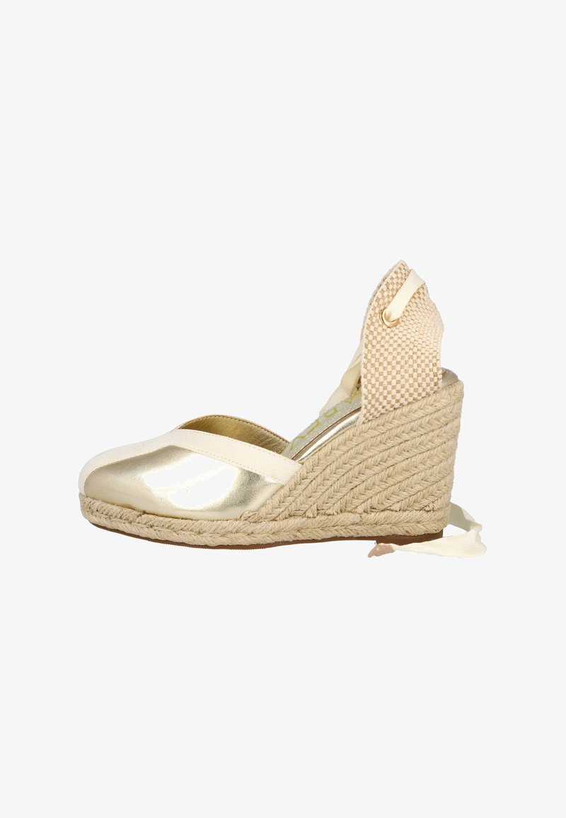 Alpargatas de cuña metálicas doradas con suela de yute trenzado. Cuentan con una correa de tela y una parte trasera texturizada con un lazo.