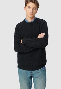 Granatowy sweter z dzianiny o teksturowanej powierzchni, z prążkowanymi mankietami i dołem. Połączony z jasnoniebieskimi dżinsami, co podkreśla swobodny styl.