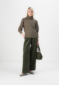 Mörk olivgrön ribbad polotröja i kombination med vida gröna kordfläskbyxor. Modellen håller en liten tygväska och bär taupefärgade ballerina-skors.