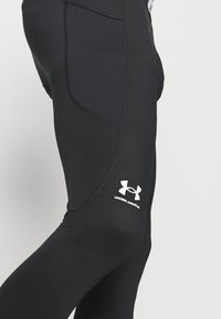 Svarte treningsleggings laget av elastisk materiale, med et teksturert panel, sidelomme og en hvit logo på det nedre benet.