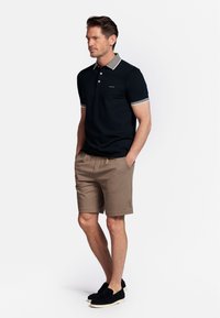 Donkerblauwe polo met een contrasterende kraag, gecombineerd met lichtbruine shorts en zwarte instapschoenen. Eenvoudig, casual ontwerp.