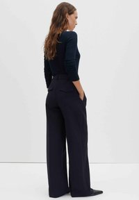 Haut bleu marine à manches longues associé à un pantalon taille haute à jambes larges. Le pantalon présente des poches arrière et une coupe ajustée pour une apparence structurée.