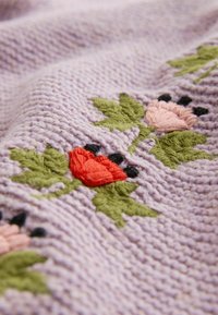 Lavendel gebreide stof met geborduurde rode en roze bloemen, groene bladeren en kleine zwarte accenten in een herhalend patroon.