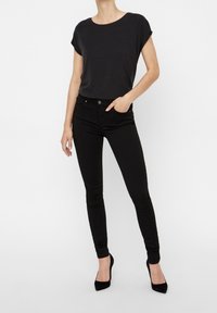 Jean noir ajusté associé à un haut noir à manches courtes. Les caractéristiques incluent un col rond, des jambes slim et des chaussures à talons hauts noires.