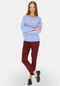 Jasnoniebieski oversize sweter z dekoltem w kształcie litery V, o teksturowanym splocie, połączony z bordowymi spodniami typu tapered oraz czarnymi mokasynami. Prosty, codzienny strój.