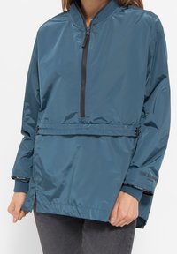 Windbreaker in teal, made of lightweight, shiny material, features a half-zip front, elastic cuffs, drawstring waist, and logo accent.