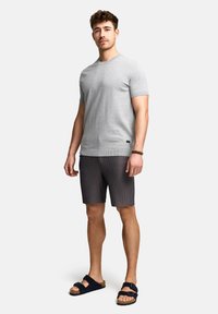 Grå kortærmet t-shirt, ribbede mørke shorts og sorte sandaler. T-shirten har en rund hals og en diskret logo-detalje ved kanten.