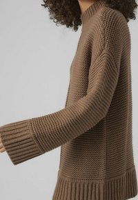 Brun stickad tröja med ribbade ärmslut och nederkant, texturerad tyg med lös passform och hög halsringning, visar sidovy och armdetalj.