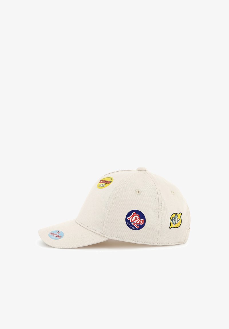 Casquette de baseball en coton crème avec une visière courbée, ornée de patchs circulaires colorés avec du texte et des logos à l'avant et sur les côtés.