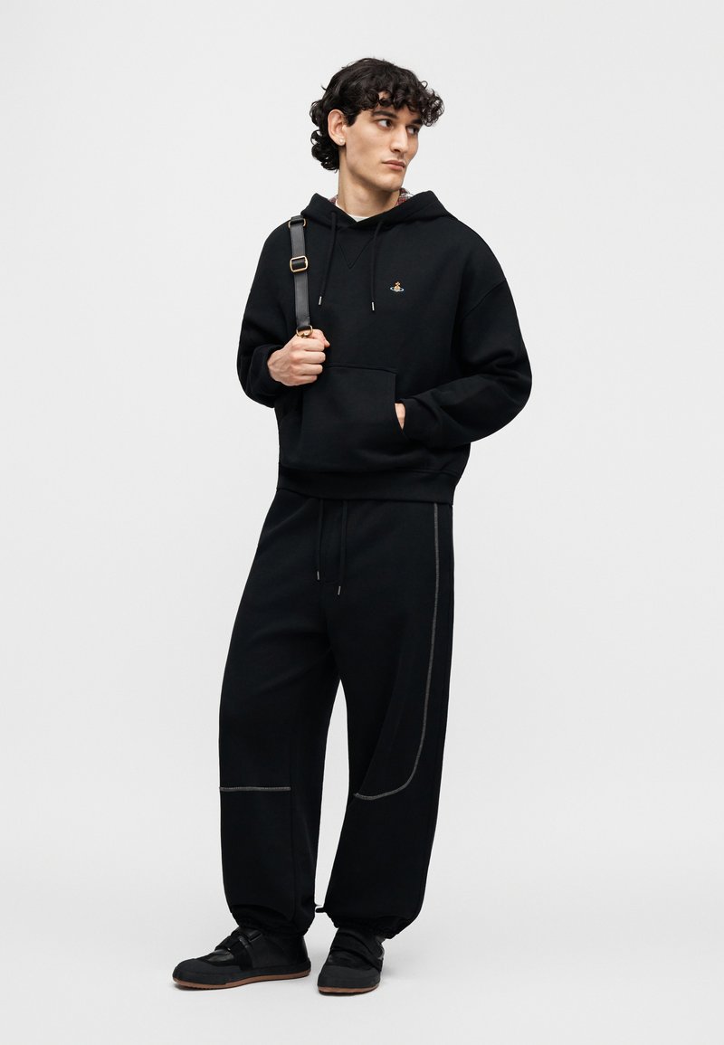 Sweat à capuche noir et pantalon de survêtement assorti en tissu doux. Le sweat à capuche comporte une poche avant et un logo discret. Le pantalon présente des coutures contrastantes.