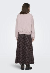 Pull rose clair avec ourlet et poignets en bord-côte, associé à une longue jupe à carreaux marron foncé. La jupe présente un motif à carreaux et une coupe fluide.