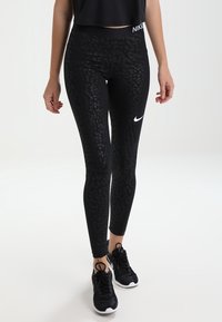 Černé legíny s texturovaným vzorem leopardího motivu, s vysokým pasem a bílým logem Nike. Spárovány s černými sportovními botami.