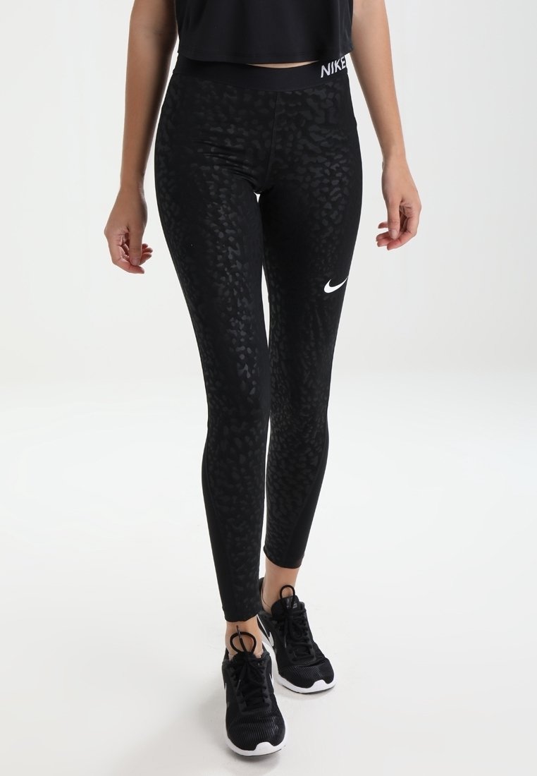 Černé legíny s texturovaným vzorem leopardího motivu, s vysokým pasem a bílým logem Nike. Spárovány s černými sportovními botami.