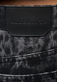 Μαύρο τζιν με υφή και καπνιστό μοτίβο, με ορθογώνια ετικέτα από υφή δέρματος με ανάγλυφο το λογότυπο "ALLSAINTS". Ορατές ραφές λεπτομέρειας.