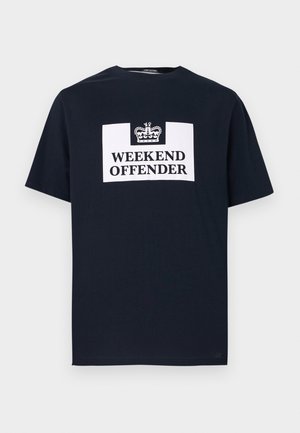 Tmavomodré tričko s bielym obdĺžnikovým logom so vzorom koruny a tučným čiernym textom „WEEKEND OFFENDER“ umiestneným v strede na prednej strane.