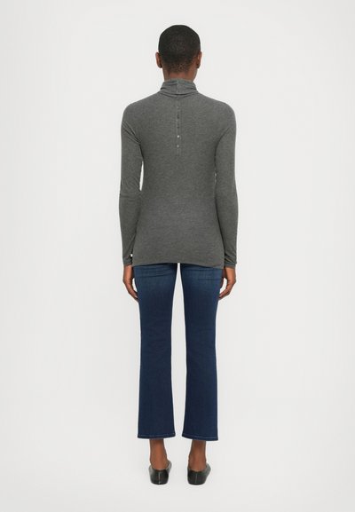 Grå langermet høyhalset genser med knappelukking bak, kombinert med blå flared jeans. Glatt stoff med lett stretch. Svarte slip-on sko.