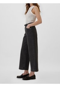 Jean noir à jambes larges avec une taille haute, associé à un débardeur blanc à rayures. Les accessoires comprennent des mocassins noirs, créant un look décontracté.