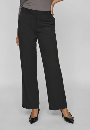 Pantalones negros ajustados con un diseño de pierna recta, que cuentan con bolsillos laterales y una textura suave. Combinados con tacones negros de punta.
