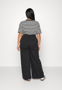 Svarta vida byxor i kombination med en randig svartvit kortärmad skjorta. Materialet verkar mjukt med en avslappnad passform.