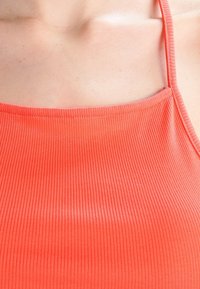 Canotta a coste con spalline sottili e scollatura a girocollo. Il tessuto è liscio con una vestibilità aderente.