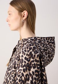 Jachetă cu glugă cu imprimeu de leopard, confecționată dintr-un material ușor și lucios. Dispune de un închidere cu nasturi și accente decorative pe glugă.