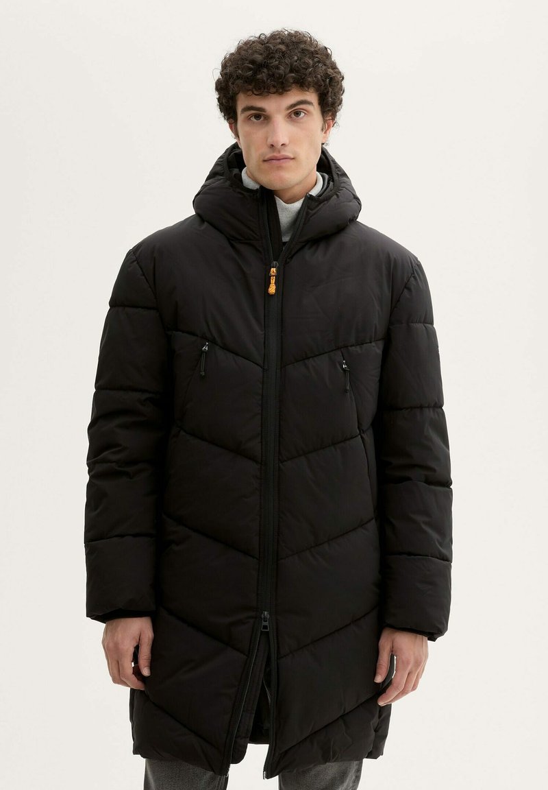 Manteau noir rembourré avec capuche, présentant des motifs de matelassage diagonaux, une fermeture éclair centrale et deux poches poitrine zippées.