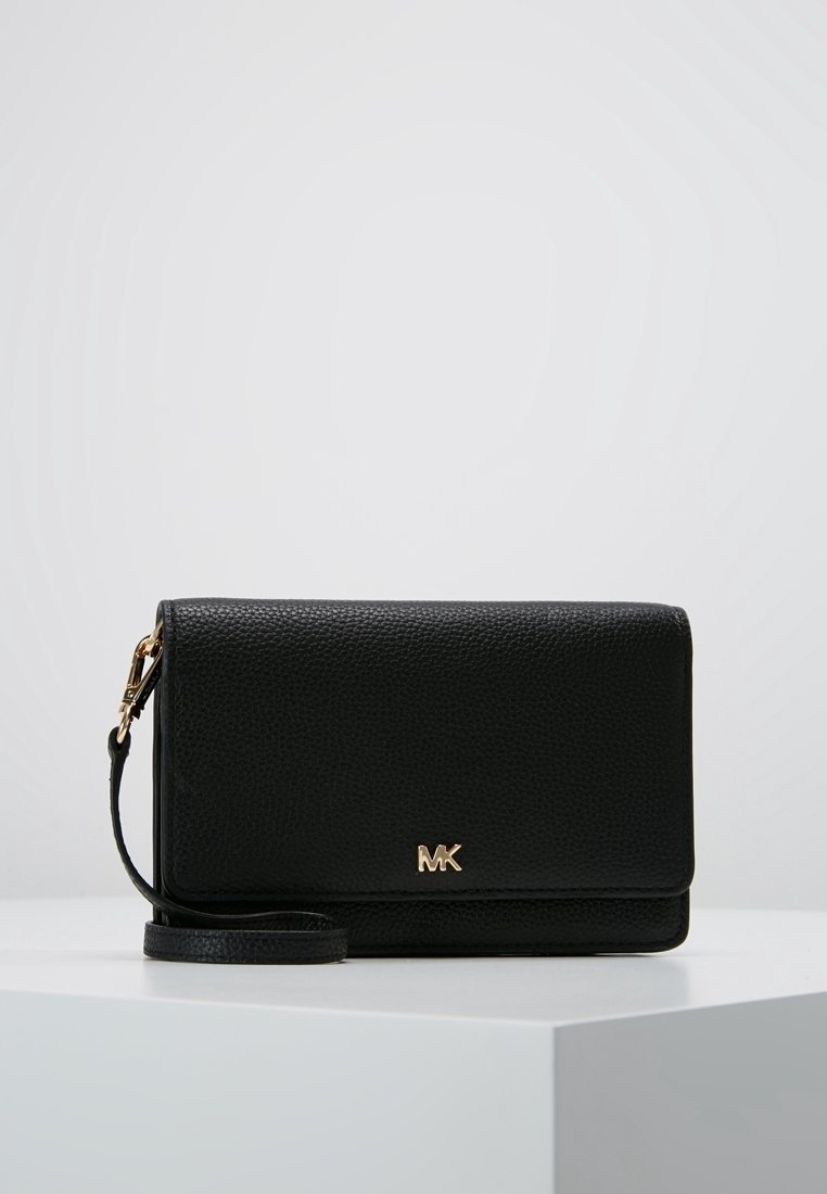 Pochette en cuir noir texturé avec logo MK doré et bandoulière amovible, présentée sur une surface blanche avec un fond uni.
