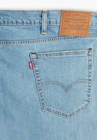 Jasnoniebieskie dżinsy z denimu o klasycznym kroju, z etykietą ze skóry na pasku, kontrastującymi przeszyciami oraz tylną kieszenią z ozdobnym zaokrągleniem.