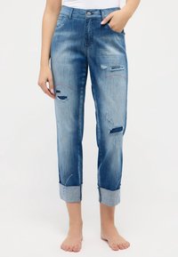 Jeans de mezclilla azul claro con detalles desgastados, puños enrollados y costura roja sutil. Cuenta con cinco bolsillos y cierre de botón.