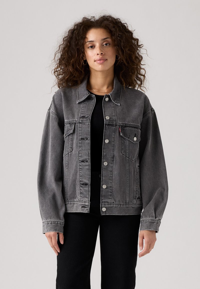 Giacca in denim grigio con collo a risvolto, chiusura con bottoni e due tasche frontali. Presenta una vestibilità comoda e dettagli di cuciture visibili.