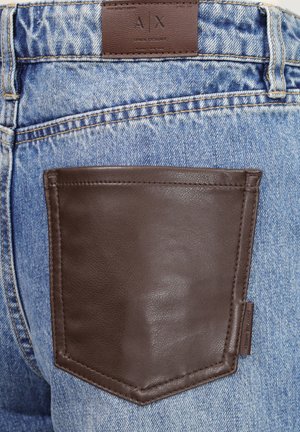Vaqueros de mezclilla azul con un gran bolsillo trasero de cuero marrón oscuro y una etiqueta de marca de cuero etiquetada A X Armani Exchange.