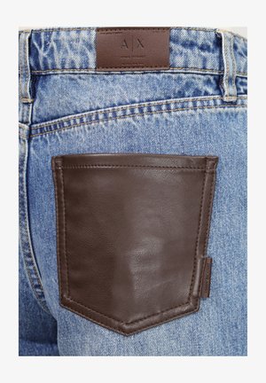 Vaqueros de mezclilla azul con un gran bolsillo trasero de cuero marrón oscuro y una etiqueta de marca de cuero etiquetada A X Armani Exchange.