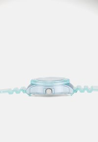 Montre bleue transparente avec un bracelet strié, un boîtier argenté et un cadran rond texturé. Présente un bouton latéral proéminent.
