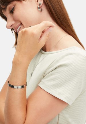Schmuckset in Silberton umfasst Creolen, ein Armband mit abwechselnden schwarzen und silbernen Segmenten sowie eine zarte Kettenhalskette.