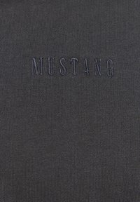Sötétszürke szövet, finom bordázott textúrával, amelyen a "MUSTANG" felirat látható, egy kicsit sötétebb szürke árnyalatban.