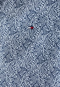 Tissu marine avec un motif paisley blanc en tourbillon. Une petite étiquette de marque avec des accents rouges, blancs et bleus est visible.