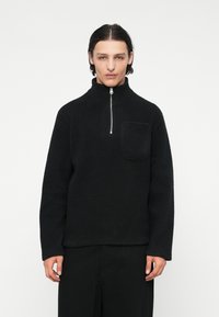 Pulover negru din fleece, cu guler înalt, fermoar pân�ă la jumătate și buzunar frontal. Caracteristici includeț țesătură texturată și croială lejeră. Mâneci lungi și design minimal.