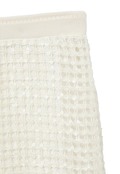 Jupe tricotée blanche présentant un design ouvert et texturé avec de petits motifs floraux, finie par une taille élastique côtelée.