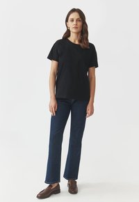 T-shirt nera a maniche corte con scollatura rotonda, abbinata a jeans svasati blu scuro e mocassini marroni. Design semplice e pulito.
