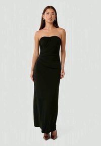 Abito maxi nero senza spalline con dettagli arricciati sul busto, realizzato in un tessuto liscio. Indossato con tacchi a punta.