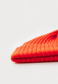 Lys orange strikket beanie-hat med ribbstrik, foldet ved kanten for en tæt pasform. Glat overflade, letvægtsmateriale.