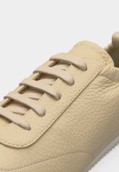 Κοντινό πλάνο μπεζ δερμάτινου σπορ παπουτσιού με υφή, με κορδόνια ίδιου χρώματος και διακριτικές λεπτομέρειες ραφών στο πάνω μέρος του παπουτσιού.