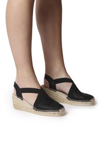 Černé pletené espadrilky na klínu s jutovou podrážkou, vybavené křížovými elastickými pásky a otevřeným designem paty pro lepší prodyšnost.
