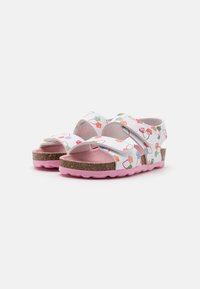 Sandalias blancas con patrón floral, correas de velcro duales, plantilla de corcho y suela de goma rosa. Diseño de punta redondeada y talón abierto.
