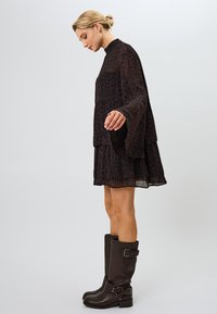 Vestido negro de tiras con un estampado de leopardo, mangas largas acampanadas y un escote alto, combinado con botas de cuero marrón hasta la rodilla.